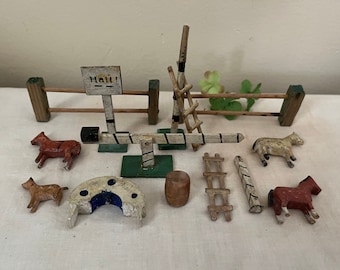 May include: A set of wooden toy horse jumping obstacles, including a gate, a seesaw, a barrel, a horseshoe, and two ladders. The set is painted in white, black, and red.