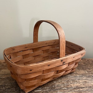 May include: A rectangular woven basket with a wooden handle. The basket is made of natural wood and has a light brown colour.