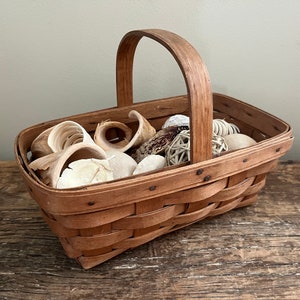 May include: A brown woven basket with a handle filled with white and brown decorative items.
