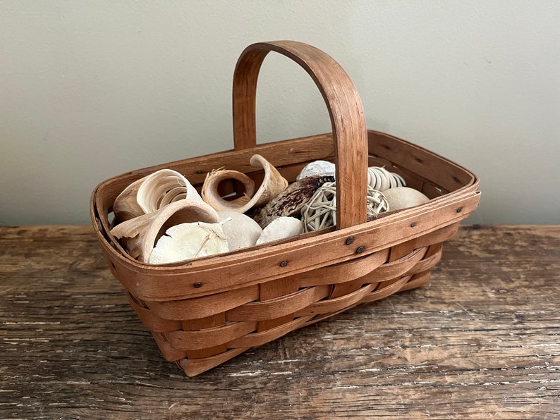 May include: A brown woven basket with a handle filled with white and brown decorative items.