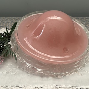 May include: A clear glass cloche with a pink glass dome. The cloche has a decorative, scalloped edge.