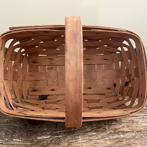 May include: A brown wooden basket with a woven design and a single handle. The basket is empty and appears to be vintage.
