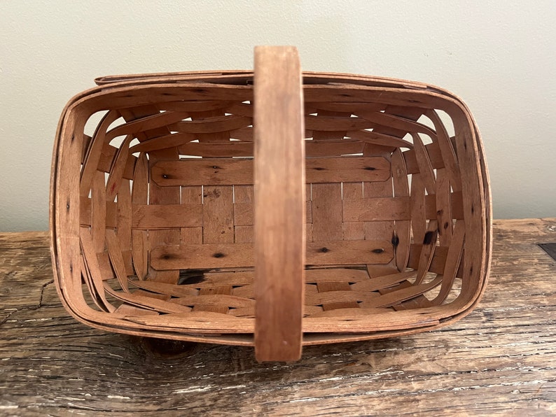 May include: A brown wooden basket with a woven design and a single handle. The basket is empty and appears to be vintage.
