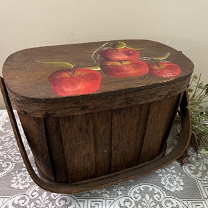 May include: A wooden basket with a hinged lid and a handle. The lid is decorated with a painting of red apples and green leaves. The basket is made of dark brown wood and has a metal handle.
