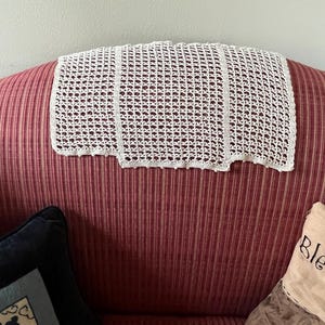 May include: A rectangular off-white crochet antimacassar featuring a repeating openwork grid pattern, vertical solid bands, and a scalloped bottom edge with small decorative bobbles along the border, designed for placement on furniture upholstery.
