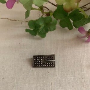 May include: A silver-toned brooch with a rectangular shape, set with black stones. The brooch has a geometric design.