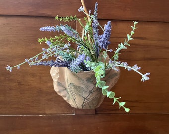 May include: A ceramic wall planter with a leafy design, holding a bouquet of purple lavender and green foliage.