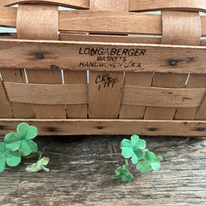 May include: A Longaberger basket made of woven wood with a label that reads "Longaberger Baskets Handwoven U.S.A." and a handwritten inscription that reads "CKL 1997".