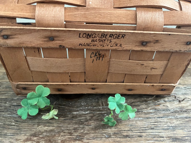 May include: A Longaberger basket made of woven wood with a label that reads "Longaberger Baskets Handwoven U.S.A." and a handwritten inscription that reads "CKL 1997".