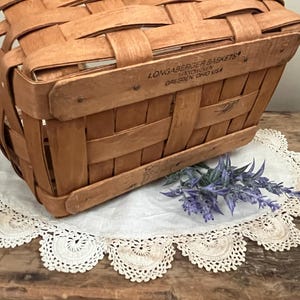 May include: A vintage wooden basket with a woven design. The basket has a label that reads "Longaberger Baskets,  Hawthorn, Dresden, Ohio USA".