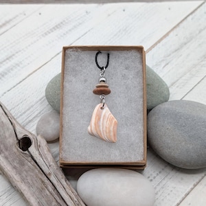 May include: A necklace pendant featuring a smooth, triangular, white and peach-colored stone suspended from a black cord. The pendant includes a small silver-toned metal bead and a flat, round, brown wooden bead above the stone.