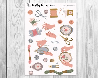 May include: A sheet of colorful stickers featuring various needlework and sewing themed illustrations. The stickers include images of spools of thread, needles, scissors, thimbles, buttons, and hands stitching. The text "The Crafty Grimalkin SS - Needlework" is at the top of the sheet.