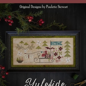 May include: A cross-stitch pattern featuring a white reindeer pulling a sleigh with a red-clad figure and gifts. The pattern is framed in a dark wood frame and has the text "Dec. 25" and "Yuleside Delivery" on the image.