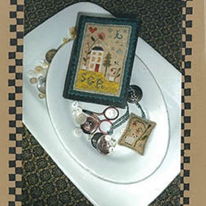 May include: A needlepoint stitch book titled "Virtue Leads Stitch Book" featuring a small needlepoint design of a house with a red heart and the text "SGB" on a white background. The design is on a blue background and is surrounded by buttons and other needlepoint supplies.