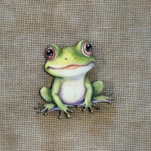 May include: A whimsical, hand-painted frog figurine. The frog is primarily green with a white belly, large brown eyes, and a smiling expression. The figurine is set against a textured, neutral-toned background, creating a charming, nature-inspired aesthetic.