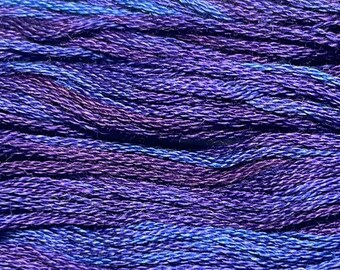 May include: A multi-ply embroidery thread featuring a variegated color palette of deep violet, royal purple, and bright cobalt blue. The fibers are tightly twisted together, creating a textured surface with a subtle sheen and distinct horizontal lines.