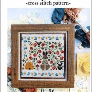 May include: A framed cross-stitch pattern titled "Berry Patch." The artwork features a brown rabbit, birds, a beehive, and red flowers. The frame is made of wood. The word "hello" is written in cursive at the bottom.