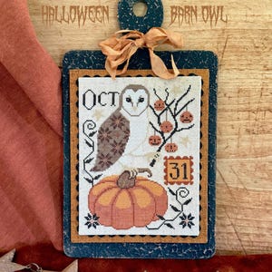 May include: A decorative wooden plaque with a stitched Halloween design. The design features an owl, pumpkin, and the text "OCT" and "31". The plaque is adorned with a peach-colored ribbon and the words "HALLOWEEN BARN OWL".