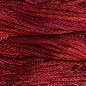 May include: A close-up view of deep red embroidery floss, showcasing the twisted strands of thread with a subtle sheen. The fibers are densely packed, creating a rich, textured surface with varying shades of dark crimson and maroon throughout.