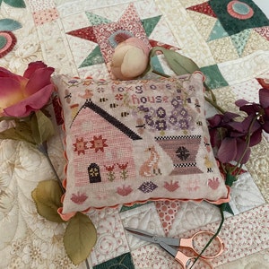 May include: A hand-stitched pillow with a pink and white floral design and the text "Foxglove House". The pillow is on a white and pink quilt with a star pattern.