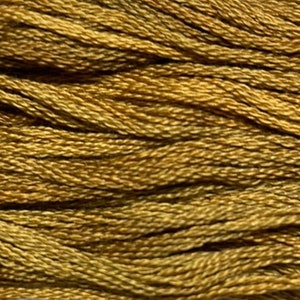 May include: Close-up of a skein of embroidery floss in shades of gold and olive green. The threads are tightly twisted, creating a textured surface. This craft supply is ideal for embroidery, cross-stitch, and other needlework projects.