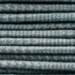 May include: Close-up of a stack of folded gray fabric. The fabric has a textured, woven pattern with a subtle herringbone design. The layers of fabric are neatly stacked, creating a sense of order and texture. The color is a muted gray.