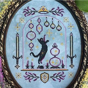 May include: A cross-stitch embroidery in an oval frame featuring a black cat reaching for a star inside an arched structure. The design includes hanging ornaments, candles, and a small mouse on a light blue fabric background with purple and gold accents.