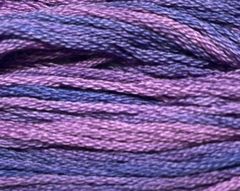 May include: A close-up view of embroidery floss featuring a variegated color palette of deep violet, royal purple, and soft lavender threads twisted together. The individual strands are tightly wound, creating a textured surface with a subtle sheen.