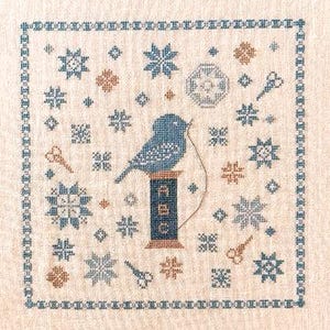 May include: Cross-stitch sampler featuring a bluebird perched atop a spool of thread labeled "ABC." The design includes snowflakes, scissors, and other decorative elements in shades of blue and brown, framed by a blue border on a beige background.