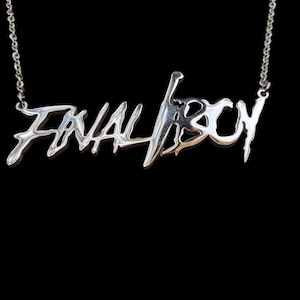Peut inclure: Un collier en argent avec un pendentif qui dit "FINAL FICTION" dans une police de caractères stylisée.