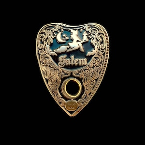 May include: A decorative planchette with a gold-colored frame and a black center. The planchette features a witch on a broom, a crescent moon, and the word "Salem". A pumpkin is at the bottom.