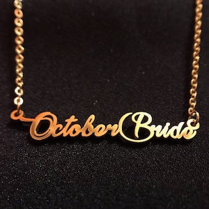 May include: Gold necklace with the words "October Bride" in a cursive font.