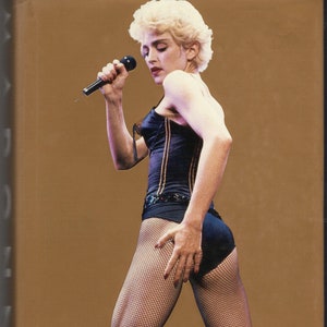 May include: A woman with blonde hair is wearing a black corset and fishnet stockings. She is holding a microphone and singing.