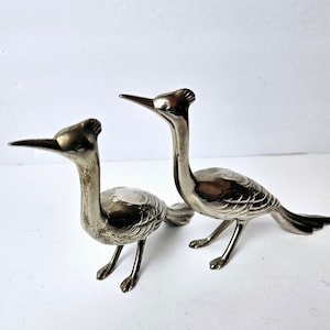 Peut inclure: Deux figurines d'oiseaux en métal argenté avec de longs cous et des plumes détaillées. Les oiseaux sont tournés dans des directions différentes et ont une apparence réaliste.