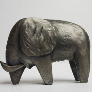 May include: A gray metal sculpture of an elephant with a textured surface. The elephant is standing on all four legs with its trunk raised.