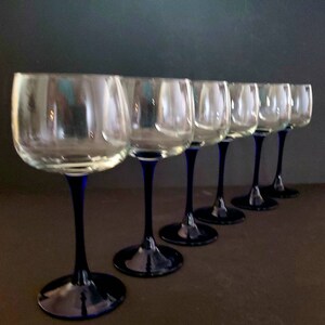 May include: Set of six clear glass wine glasses with blue stems. The glasses are arranged in a row, with the stems pointing towards the right.