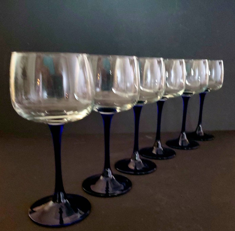 May include: Set of six clear glass wine glasses with blue stems. The glasses are arranged in a row, with the stems pointing towards the right.