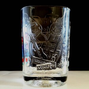 May include: Clear glass cup with a design of a guitar, a building, and the words "Hollywood Vine" etched into the side. The bottom of the cup has the words "Disney World" etched into it.