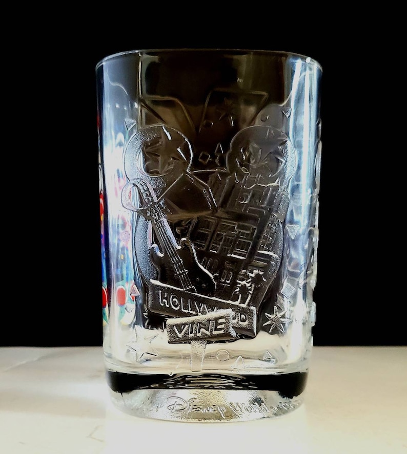 May include: Clear glass cup with a design of a guitar, a building, and the words "Hollywood Vine" etched into the side. The bottom of the cup has the words "Disney World" etched into it.