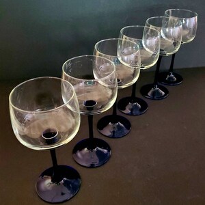 May include: Set of six clear glass wine glasses with dark blue stems and bases. The glasses are arranged in a row, with the stems pointing to the right.