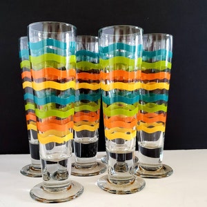 Puede incluir: Juego de seis vasos altos de vidrio transparente con diseños coloridos a rayas. Las rayas son de color naranja, amarillo, verde y azul.
