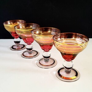 May include: Set of four clear glass cocktail glasses with a red base and gold and white striped accents.