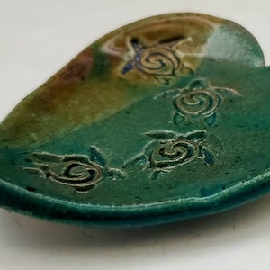 May include: A green ceramic dish with a heart shape and a raised design of four sea turtles. The dish has a brown and green glaze.