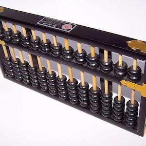 Puede incluir: Un ábaco negro tradicional con varillas de madera y cuentas negras. El marco es negro con detalles de esquina de latón. Esta herramienta de cálculo se utiliza para cálculos aritméticos. Mide unos 30 cm de largo.