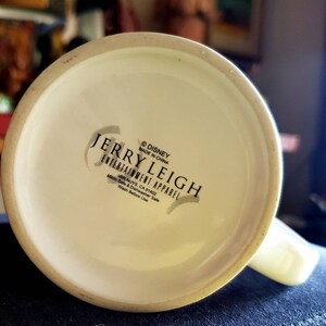 May include: White ceramic mug with a black and white logo that reads "&copy;DISNEY MADE IN CHINA JERRY LEIGH ENTERTAINMENT APPAREL VAN NUYS, CA 91402 Micro Safe & Dishwasher Safe Wash Before Use"