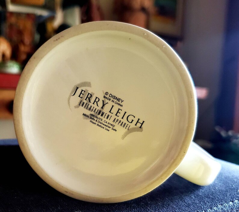 May include: White ceramic mug with a black and white logo that reads "&copy;DISNEY MADE IN CHINA JERRY LEIGH ENTERTAINMENT APPAREL VAN NUYS, CA 91402 Micro Safe & Dishwasher Safe Wash Before Use"
