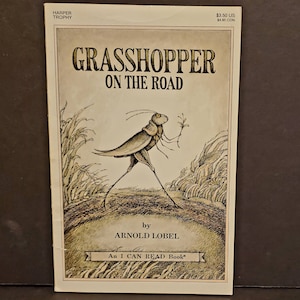 Könnte beinhalten: Ein Vintage-Kinderbuchcover mit einem Cartoon-Grashüpfer, der auf einem Weg mit einer Blume in der Hand geht. Der Titel des Buches lautet "Grasshopper on the Road" von Arnold Lobel. Das Buch ist Teil der Reihe "I Can Read Book".