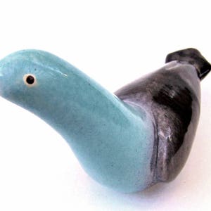 May include: A ceramic bird ornament with a light blue head and neck, fading into a dark grey body. The bird has a black beak and a small, round eye. This is a decorative item.