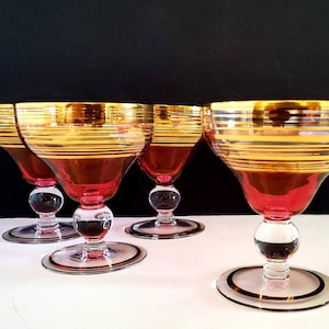 Peut inclure: Ensemble de quatre verres à cocktail en verre rouge à pied avec des rayures dorées et argentées autour du bord et du bol.
