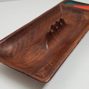 May include: A wooden ashtray with a rectangular shape and a carved out area for cigarettes. The ashtray has a green and orange glaze on the side.
